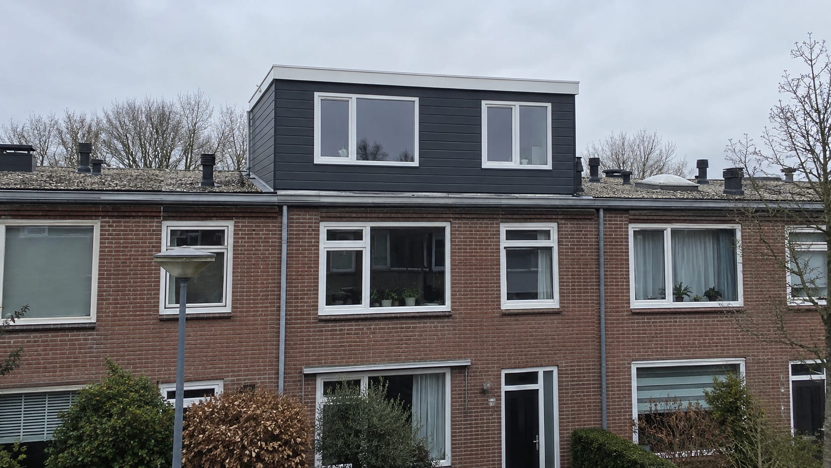 Rijwoningen waarvan één woning voorzien is van een nieuwe dakopbouw met donkere gevelbekleding